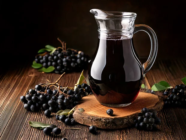 Glaskaraffe mit Aroniabeeren-Saft auf einem Holzuntergrund. Dekorativ Aroniabeeren und Blätter ringsherum.
