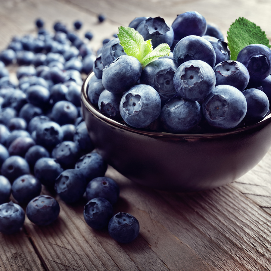 Schale mit Heidelbeeren und Minzblättern auf einem Holztisch, daneben lose Heidelbeeren.
